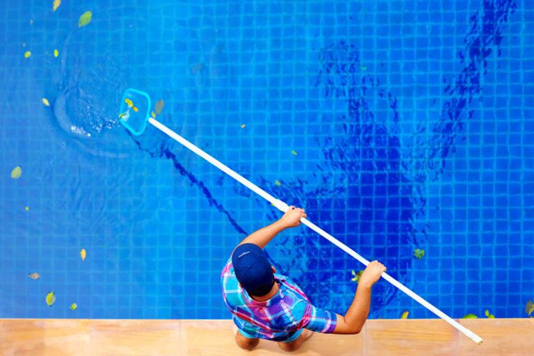 Top view of young man cleaning the pool with a pool skimmer
