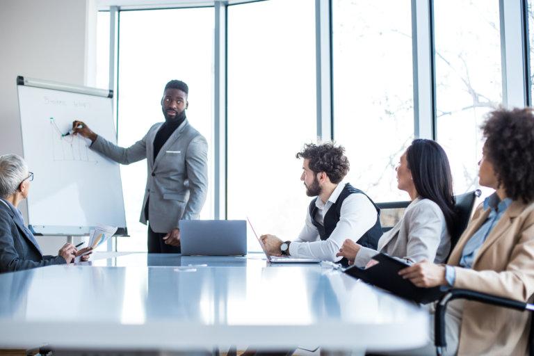 man speaking at whiteboard with coworkers