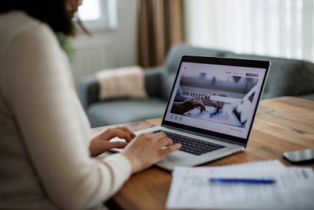 Person sitting at a desk in a home setting, using a laptop to search for a job online
