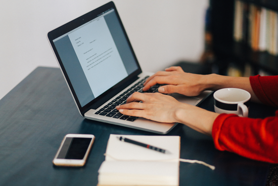 A person sitting at a desk typing a letter on a laptop, representing a professional follow-up letter expressing continued interest after a job interview.
