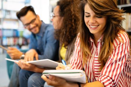 Psychology students in a positive academic setting, smiling and talking to each other while reading or writing in notebooks