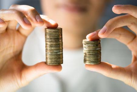 Two hands holding stacks of coins, with one stack visibly taller than the other, symbolizing the pay gap between men and women.