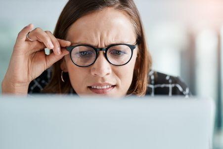 Reading a job description, a skeptical woman with glasses looks intensely at her laptop with a furrowed brow.
