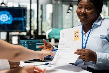 A hiring team discusses a candidate's resume, while a computer displaying AI screening technology sits in the background.