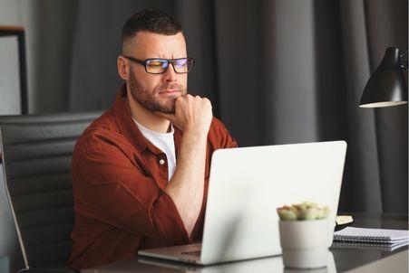 A skeptical job seeker holding their chin while cautiously evaluating a suspicious online job posting on a laptop.