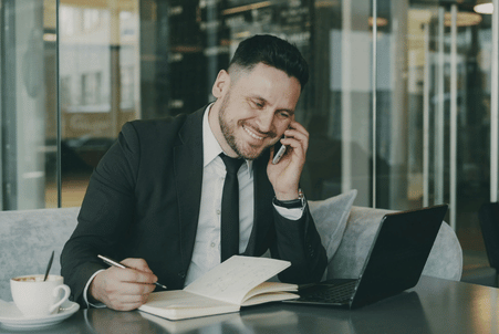 Smiling businessman taking a phone call while filling out a new business application at his laptop.